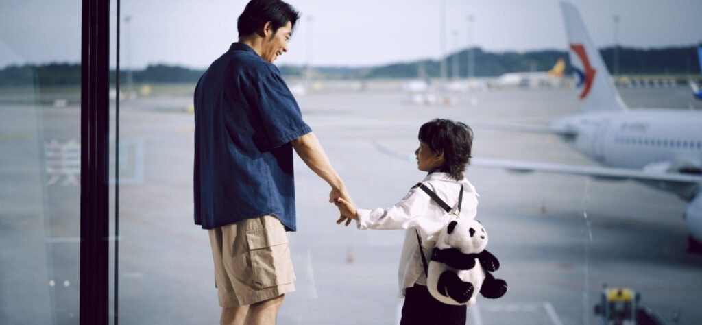 공항 터미널 큰 유리창 너머로 비행기를 바라보며 서로 손을 잡고 서 있는 아빠와 아이의 모습