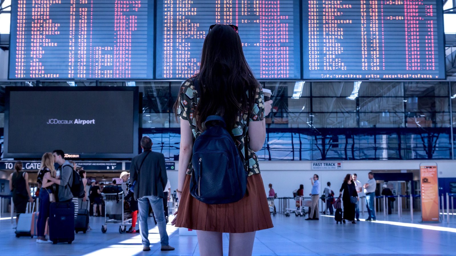 공항 터미널에서 대형 비행기 운항 정보 전광판을 바라보며 일정을 확인하는 여행객의 뒷모습